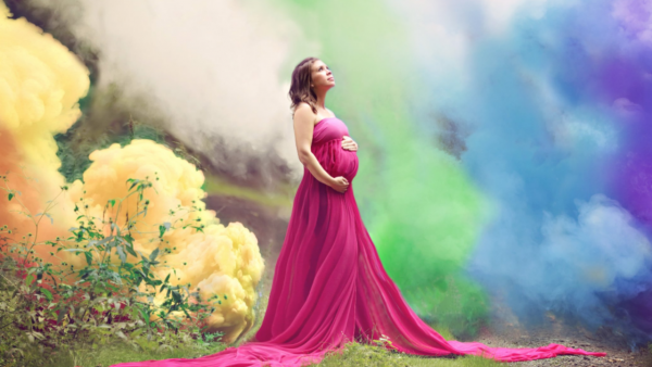 Pregnant women holding belly with rainbow clouds in the background