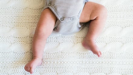 A baby with chubby little legs lying on a bed
