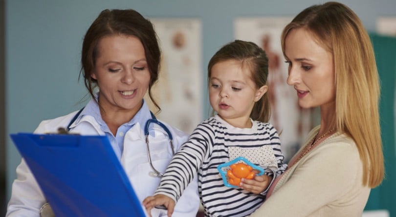 Doctor, mom and young child look onto the doctors notes in the ER