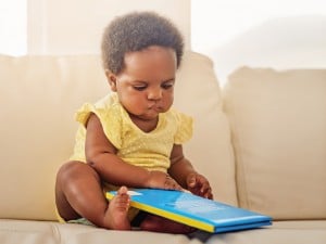 Baby sits on couch with a book