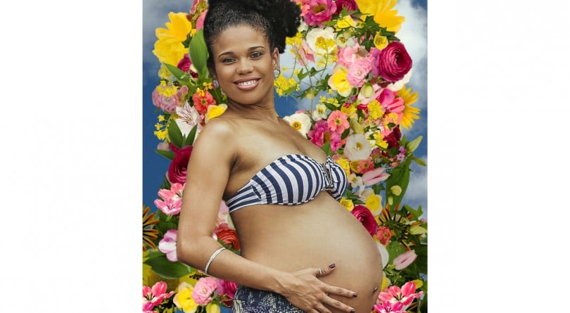 Pregnant woman in a bikini top holding her belly in front of a floral background