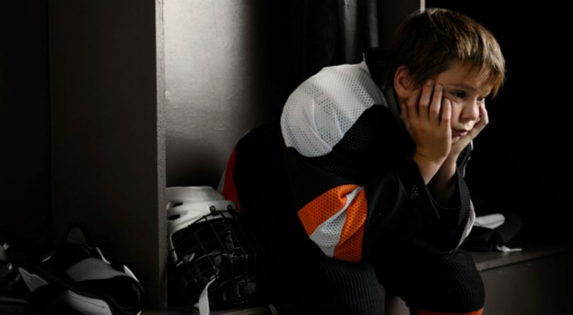 Child in hockey uniform sitting disappointed in locker room