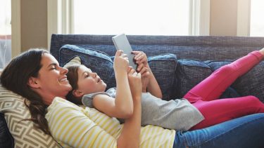 A mom and daughter laying on the couch looking at the tablet
