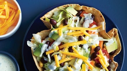 tortilla bowl filled with lettuce, tomatoes, beans and cheese