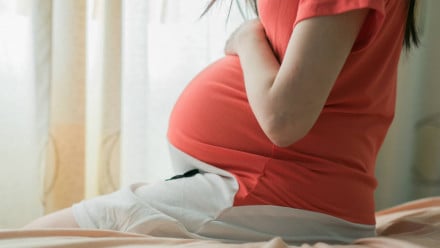 A pregnant woman sitting on the bed with her hand on her belly