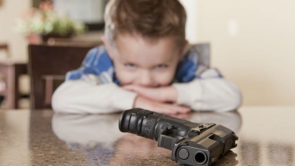 Young child looking at gun on a table
