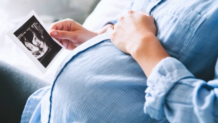 A pregnant woman holding her belly and looking at an ultrasound photo