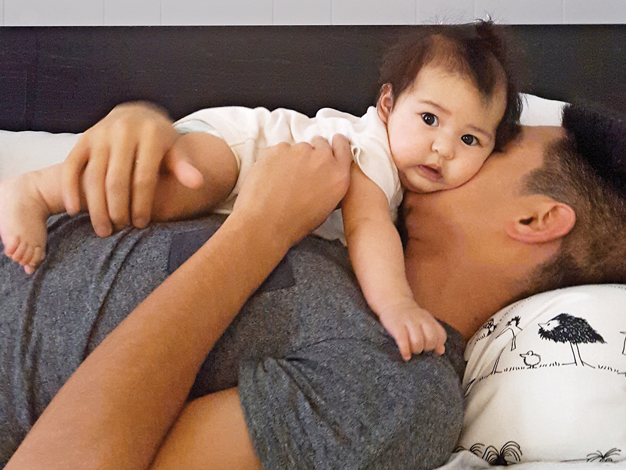 Dad lays in bed with baby daughter laying on top of him