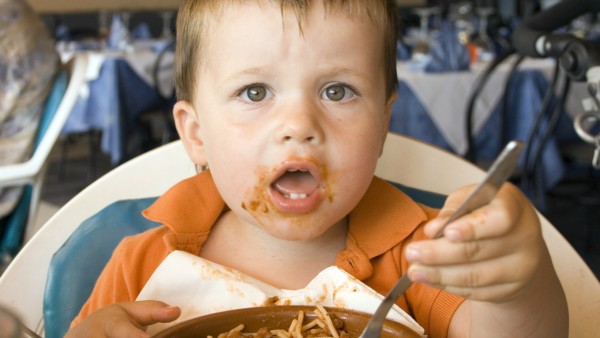 Young boy messily eating a bowl of pasta in a fancy restaurant