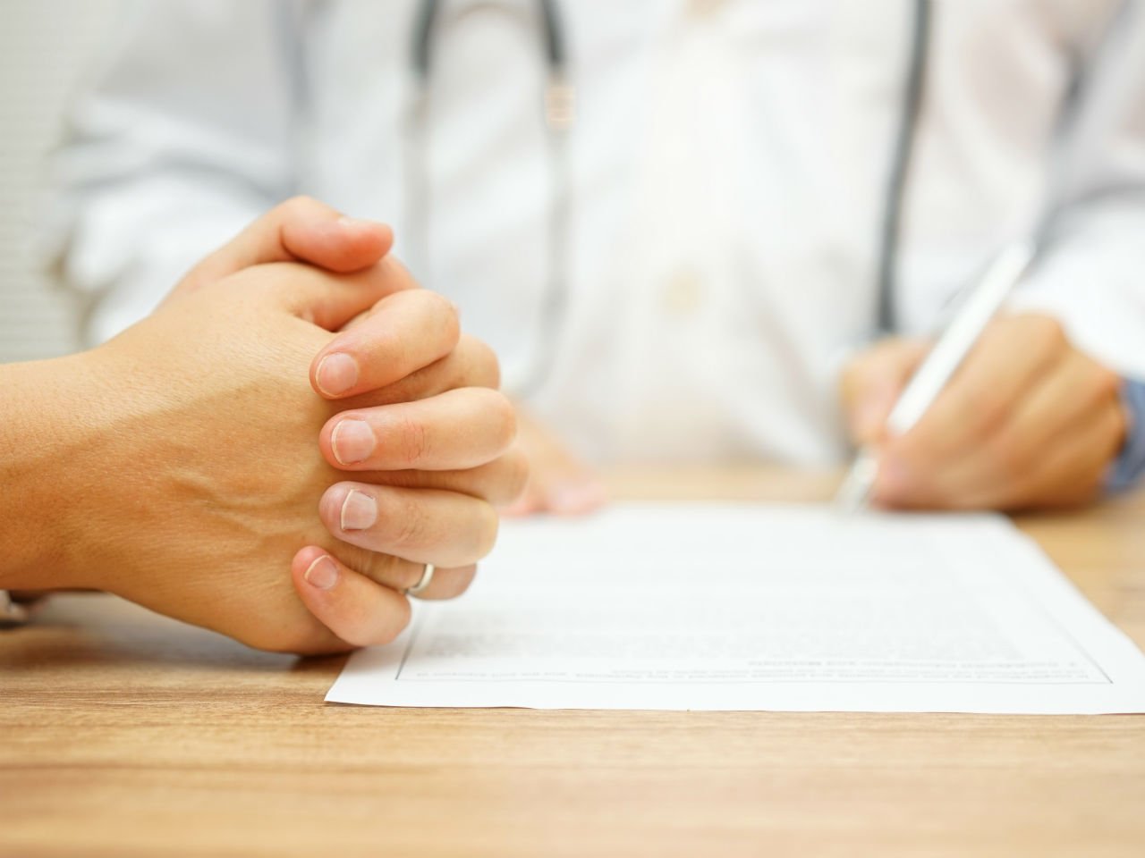 Hands clasped in front of a doctor with a medical form