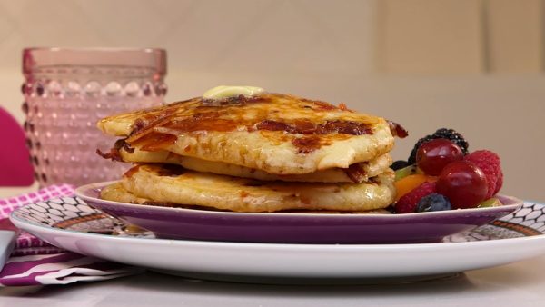 Stack of bacon pancakes with butter, syrup and fruit