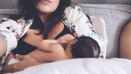 A mom breastfeeding her baby in bed on a nursing pillow