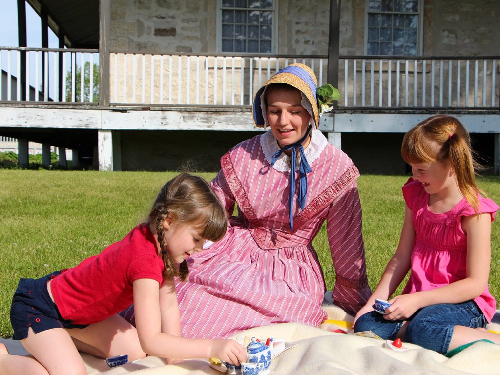 kids having a picnic with woman dressed in historic dress