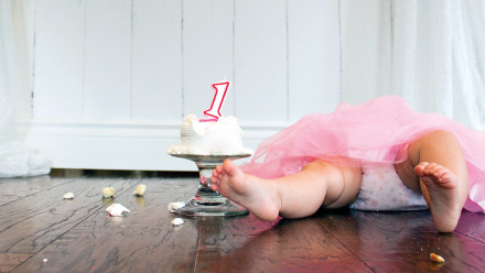 Baby laying on the floor with a crumbled first birthday cake