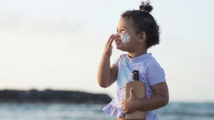 Toddler putting sunscreen on her face