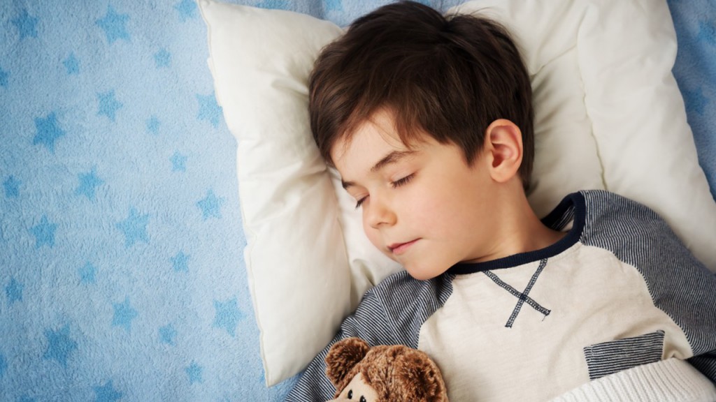 Child sleeping in bed with a brown teddy bear and blue star-patterned blanket trying to prevent bedwetting