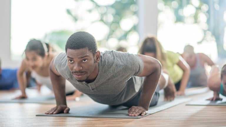 Young guy holding plank position in yoga class
