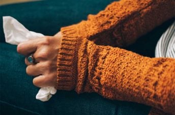 Close up of a woman's hands wearing an orange sweater holding a tissue