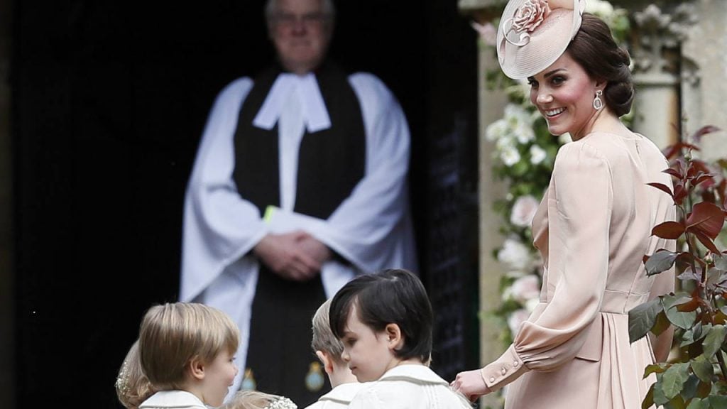 Kate Middleton in a pink dress and hat guiding the kids into Pippa's wedding