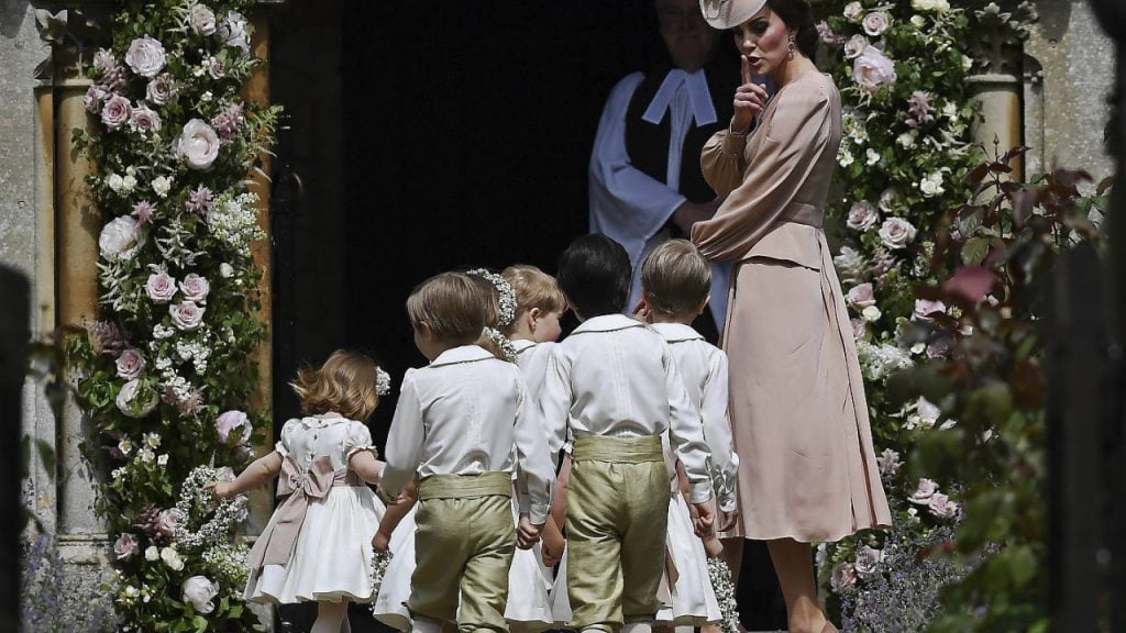 Kate Middleton in a pink dress and hat shushing the kids