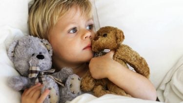 A little boy in bed cuddling his teddy bears because he's not feeling well