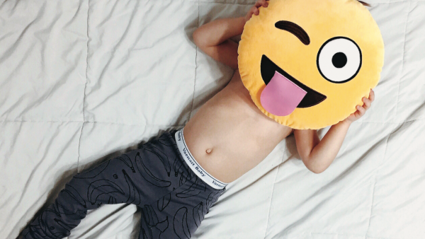 A little boy holding an emoji pillow over his face