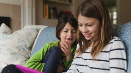 Two kids sitting on a couch, looking at a tablet