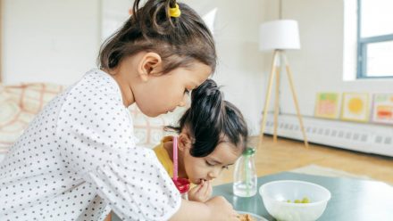 two little girls eating snacks off a table