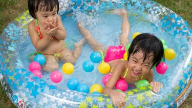 Two little girls playing in a blow up pool with neon balls