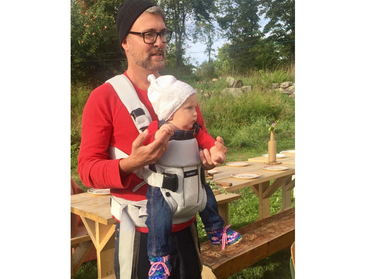 A father carries baby in a carrier at an outdoor picnic