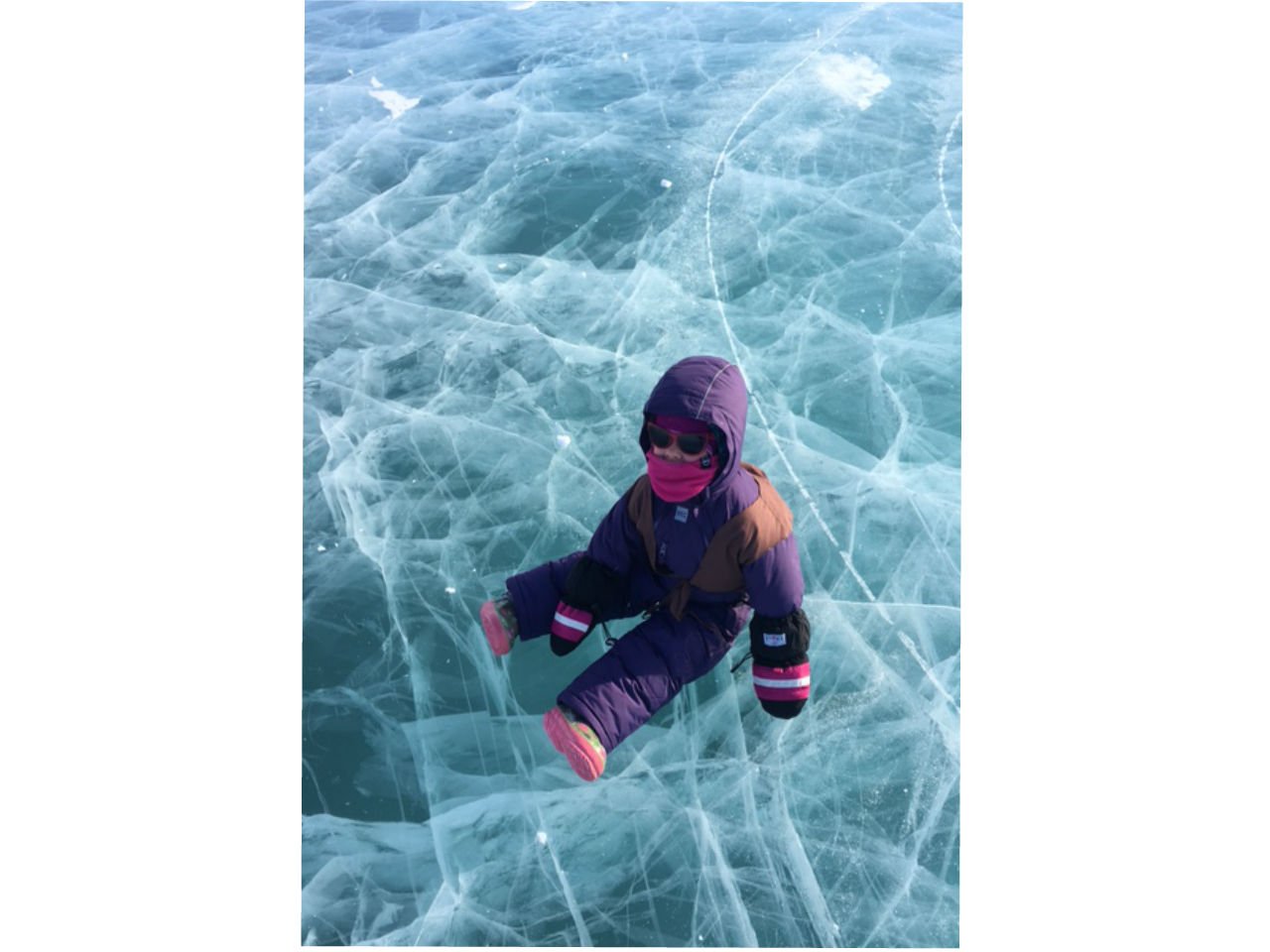 a little girl sits in a snowsuit on the ice