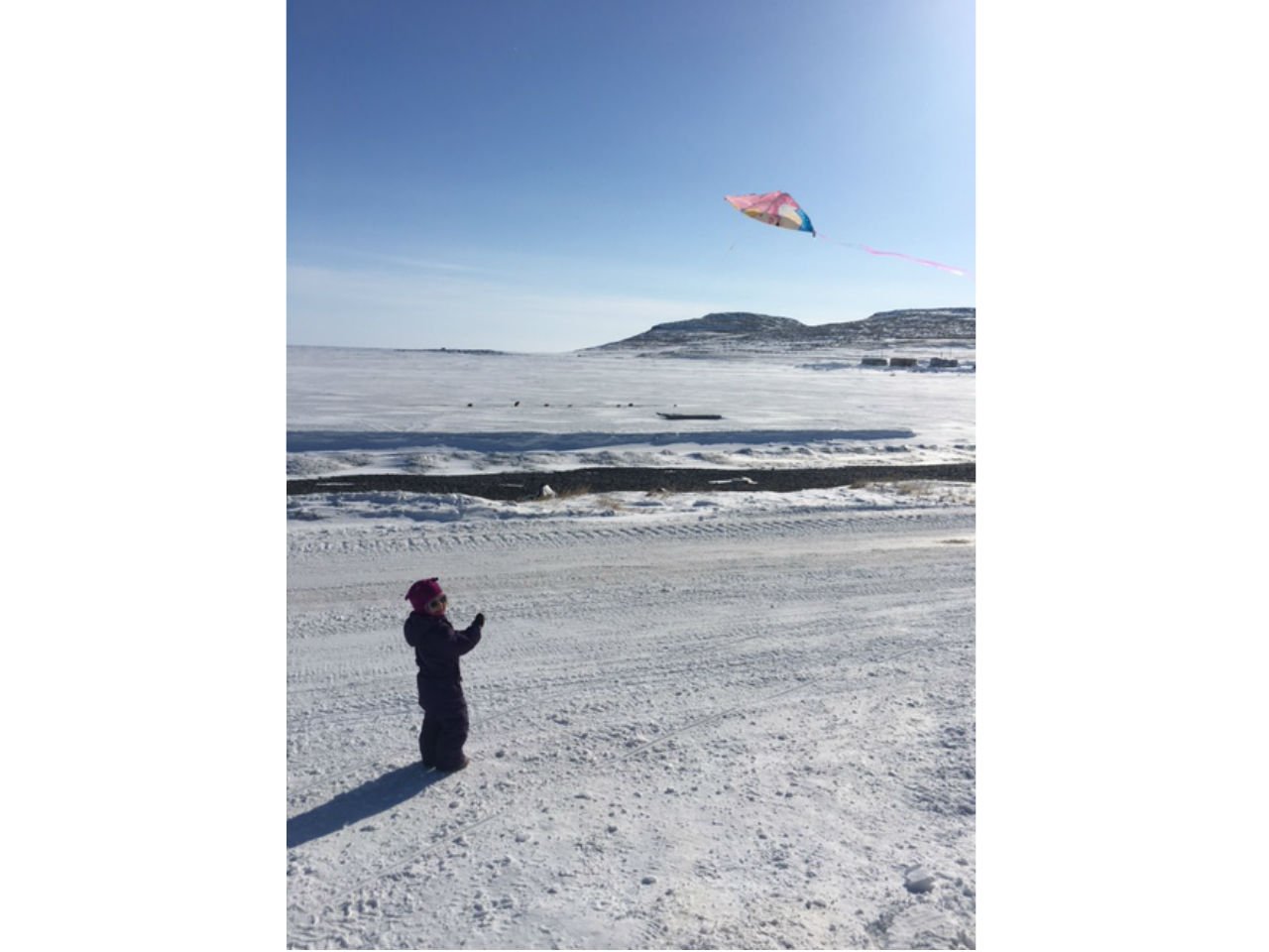 a little girl flies a kite in the winter in a snowy field