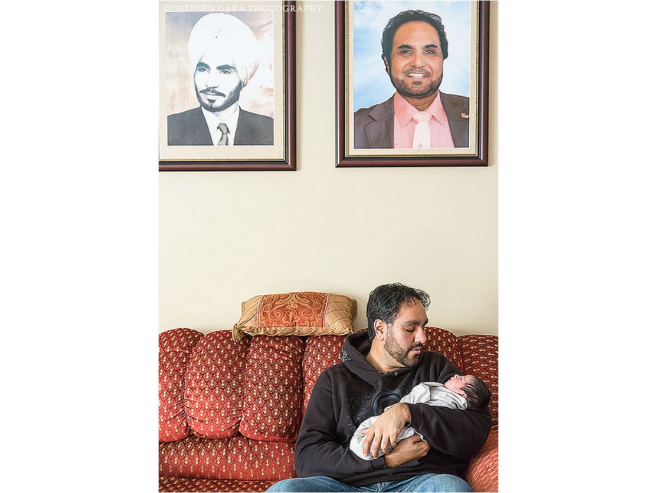 a father holds his new child beneath the portrait of his father