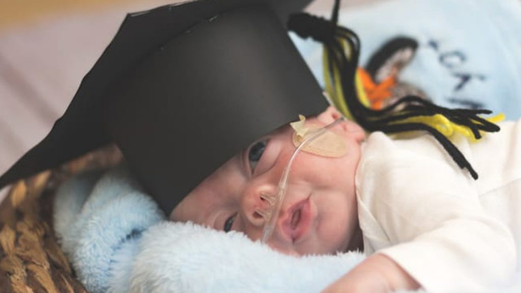 Baby with breathing tube wearing a graduation cap