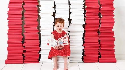 girl in red dress sitting in front of stacks of red and white books, reading 'Red is Best'