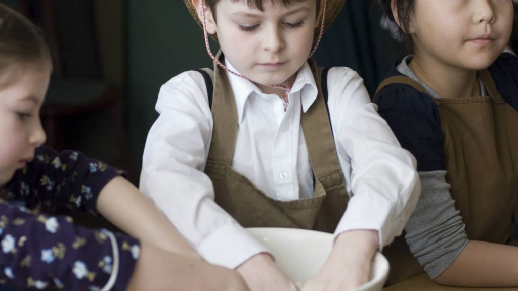 A little boy dressed as a pioneer with his hands in a bowl