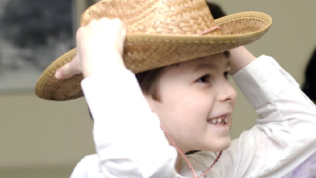 A little boy smiling while putting on a straw hat