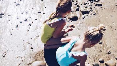 Two little girl playing on the beach with rocks