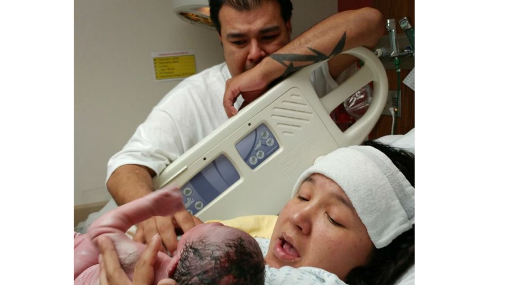 a new father watches as his partner hold their new baby for the first time