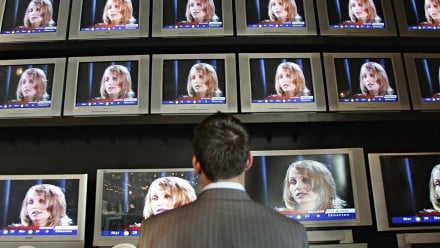 a man facing a wall of screens with Homolka's face on them