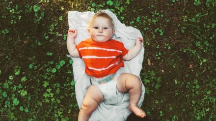 baby in a diaper laying on a blanket in a field of clovers