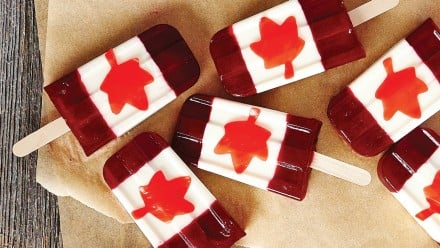 Red and white popsicles with maple leafs on them lying on parchment paper