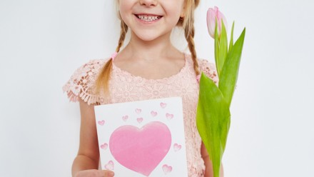 little girl holding a handmade card with heart and a pink tulip