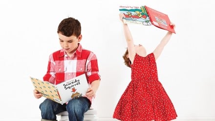 two kids sitting on a stack of books and reading