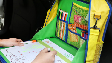 A green in-car art lap table being used by a young child