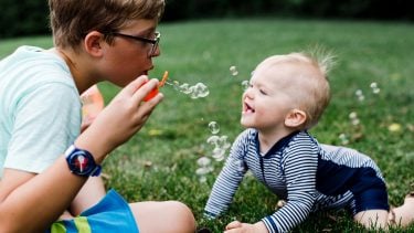 Young boy and his baby brother enjoying summer outdoors with bubbles