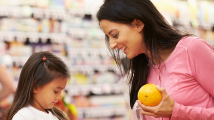 mother and daughter shopping for oranges at grocery store