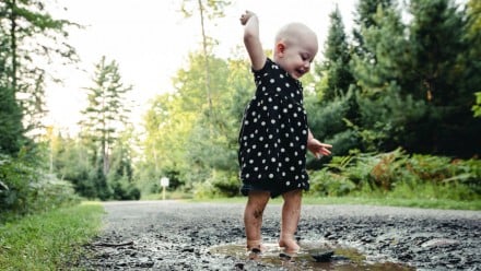 A little girl in a dress jumping in the mud