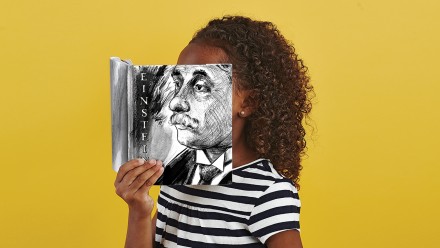 Girl holding a book in front of her face that has Einstein's face on it.