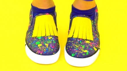 pair of slip-on shoes with paint splatter and yellow fringe